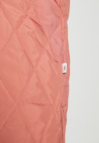 Giacca leggera trapuntata in tessuto corallo con una texture liscia e cuciture visibili. Presenta l'etichetta del marchio sulla cucitura laterale.