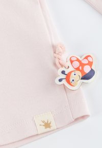 Helle rosa Baumwoll-T-Shirt mit geripptem Textil, ausgestattet mit einem bunten Marienkäfer-Tag und einem kleinen Stoffetikett mit einem Farbspritz-Design.