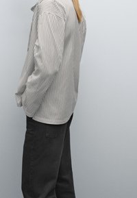 Gestreiftes Hemd aus hellgrauem und dunkelgrauem Stoff, mit Knopfrahmen, langen Ärmeln und legerer Passform, kombiniert mit dunkler Hose.