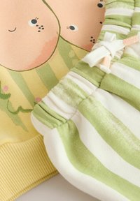 Hanorac galben cu imprimeu de desen animat și pantaloni scurți verzi cu dungi, având talie elastică și detaliu cu șnur. Material moale din bumbac vizibil.