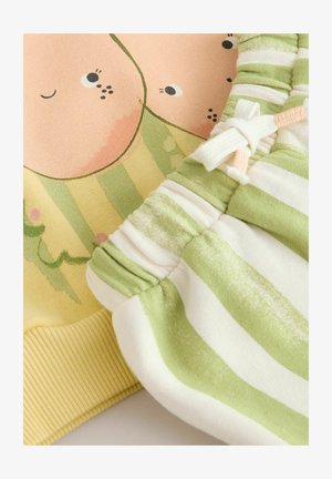 Žlutá mikina s kresleným potiskem a zelené pruhované kraťasy s elastickým pasem a mašlí. Viditelná jemná bavlněná látka.