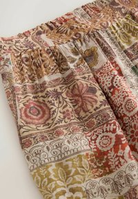 Tissu patchwork avec taille élastique, présentant des motifs floraux et géométriques dans des tons terreux de brun, rouge, vert et beige.