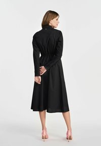 Czarna sukienka z długim rękawem, dopasowana w talii z rozkloszowanym dołem. Posiada kołnierzyk, guziki oraz gładką fakturę. Noszona z różowymi szpilkami.