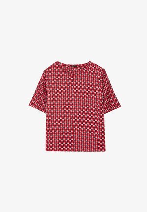 Haut rouge à manches courtes avec un motif géométrique de triangles en blanc et noir. Fabriqué en tissu lisse et léger avec un col rond.