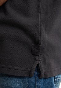 Czarna koszula z teksturowanej tkaniny z bocznym rozcięciem. Posiada prostokątną metkę z logo "Petrol Ind" w pobliżu dolnej krawędzi.