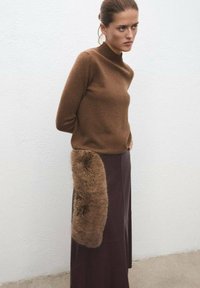 Un pull en laine marron à col roulé associé à une jupe longue marron foncé avec un long accent en fausse fourrure sur le côté.