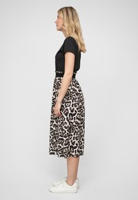 Midi sukně s leopardím potiskem a černým pasem, v kombinaci s upnutým černým tričkem. Bílé tenisky dokončují ležérní outfit.