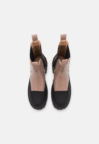 Nilkkurit, joissa on kiiltävä beige päällinen, musta kumipohja ja vetotappi. Suunnittelussa on sulavalinjainen siluetti, jossa on elastiset sivupaneelit.