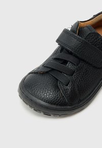 Μαύρο δερμάτινο παπούτσι με υφή στην επιφάνεια, φαρδιά λουρίδα με βέλκρο, και μαύρους κορδόνια, με στρογγυλεμένη μύτη και ανθεκτική λαστιχένια σόλα.