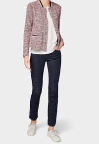 Texturiertes rosa-weißes Tweed-Jackett mit Rundhalsausschnitt und Taschen, kombiniert mit einem weißen Oberteil und dunklen Jeans, abgerundet mit weißen Sneakern.