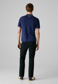Marineblauwe polo met een witte kraag en strepen, korte mouwen, logo op de achterkant, gecombineerd met donkere jeans en witte sneakers met blauwe en rode accenten.