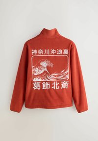 Piros polár pulóver magas gallérral. Hátul fehér hullámgrafikával és szöveggel. Puha tapintású, laza szabású, hosszú ujjú.