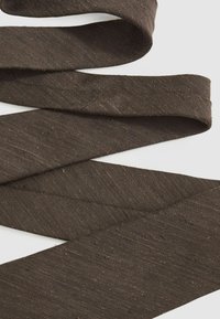 Cinta de tela marrón con un tejido texturizado, que muestra ligeras variaciones en el color y pequeñas imperfecciones, retorcida en bucles sobre un fondo blanco.