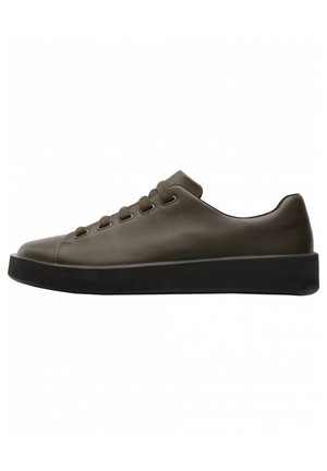 Niski brązowy skórzany sneaker z zaokrąglonym noskiem, pięcioma oczkami na sznurowadła w dopasowanym kolorze oraz grubą czarną gumową podeszwą.