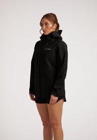 Giacca impermeabile nera con zip frontale, cappuccio regolabile e due tasche laterali. Texture liscia e design minimalista.