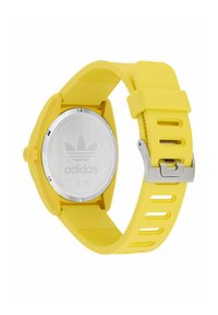 Reloj de silicona amarillo con una caja redonda de acero inoxidable, una correa texturizada y un cierre plateado, con el logo de Adidas en la parte posterior.