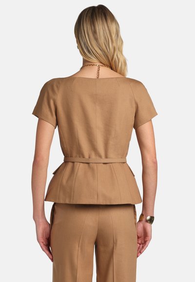 Woman with blonde hair wearing a tan short-sleeve belted top and matching pants, shown from the back against a plain background.