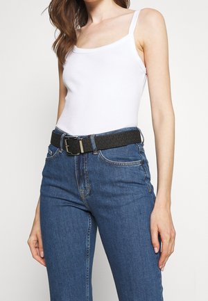 Biały prążkowany top na ramiączkach w połączeniu z niebieskimi dżinsami, wyposażony w teksturowany czarny pasek z srebrną klamrą. Strój ma swobodny krój.