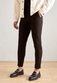 Černé slim-fit kalhoty s hladkou texturou, doplněné o tmavé mokasíny s kovovými detaily a krémovou džínovou bundou.