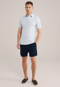 Camisa polo de color azul claro con un patrón de diamante texturizado, combinada con pantalones cortos azul marino y zapatos oscuros tipo slip-on. Diseño simple y casual.