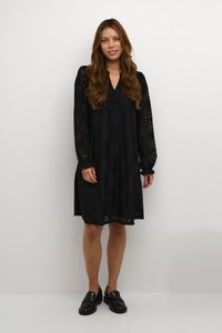 Zwarte kanten jurk met lange mouwen, een V-hals en een ingewikkeld bloempatroon. Gecombineerd met zwarte loafers voor een complete look.