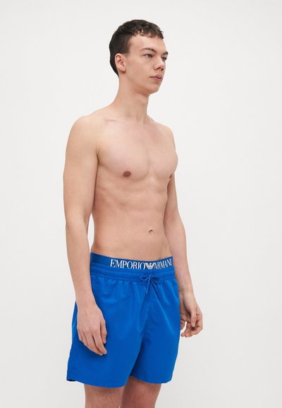 Shorts de bain bleus en tissu léger, dotés d'une taille élastique avec cordon de serrage et d'un détail de logo. Longueur mi-cuisse.