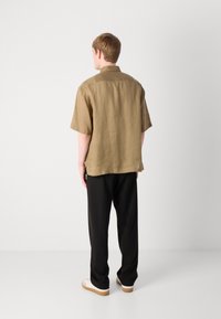 Korte mouw, olijfgroene linnen overhemd met een knoopsluiting aan de kraag, gecombineerd met zwarte broek en witte sneakers. Gladde textuur, casual pasvorm.