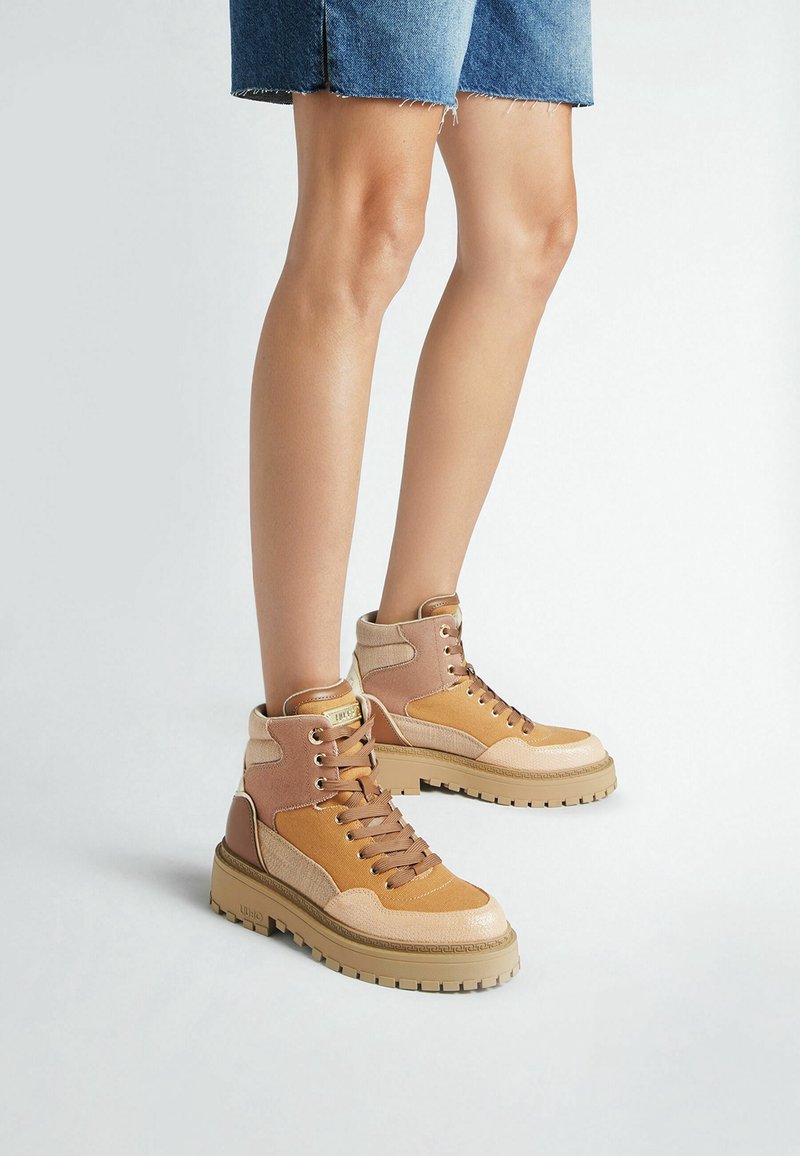 Jambes portant une jupe en jean à ourlet effiloché et des bottines à plateforme marron clair à lacets avec des panneaux en daim et cuir mélangés.