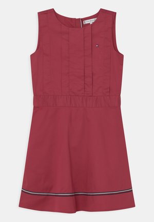 Vestido sin mangas en tela de color rojo oscuro con pliegues verticales y una costura en la cintura. Presenta una franja de contraste en el dobladillo. Cierre trasero con cremallera.