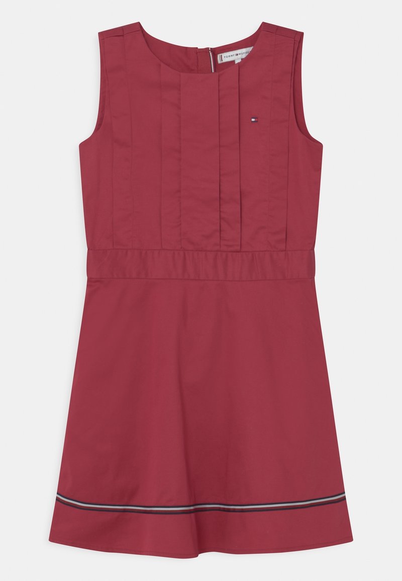 Robe sans manches en tissu rouge foncé avec des plis verticaux et une couture à la taille. Elle présente une bande contrastante à l'ourlet. Fermeture zippée au dos.