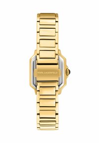 Gouden horloge met rechthoekige wijzerplaat, geborstelde en gepolijste schakels, en een zwarte kroon. Heeft een gegraveerde merknaam aan de achterkant.