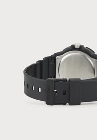 Montre bracelet en caoutchouc noir avec un boîtier rond en acier inoxydable. Présente un bracelet texturé et une boucle en métal avec "CASIO" embossé.