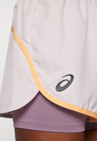 Világoslila sportderekú szoknya narancssárga varrással és fekete logóval; levél formájú, levendulaszínű sortokra rétegezve, puha anyagból és íves szegéllyel.