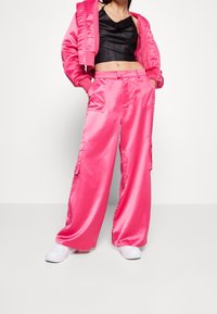 Rosa satin träningsdräkt bestående av en kort jacka och byxor med vida ben, med sidofickor och en jämn, glänsande yta.