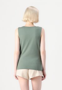Ermeløs grønn topp laget av myk stoff, med rund hals og tettsittende fasong, paret med lyse beige shorts.