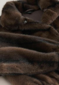 Brown faux fur coat featuring a soft, plush texture, wide collar, and curved edges, highlighting a sleek design with subtle color variations.