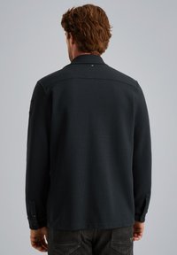 Temno modra srajca z dolgimi rokavi, z teksturirano obliko, z gumbi na manšitah in enim logotipom na hrbtu blizu ovratnika.