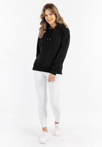 Fekete kapucnis pulli puha anyagból, zsinórral, bordázott mandzsettákkal és aljjal. Fehér skinny farmernadrággal és fehér tornacipővel párosítva.