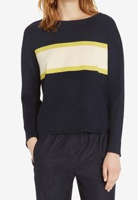 Maglione a maniche lunghe blu navy con una striscia orizzontale crema e gialla sul petto. Tessuto morbido, forma rilassata e scollatura rotonda.