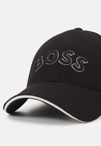 Schwarze Mütze aus strukturiertem Stoff, mit einem gestickten "BOSS"-Logo in Weiß und einem weißen Akzent auf dem gebogenen Schirm.