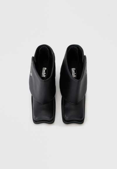 Botine negre până la gleznă din piele netedă, cu vârf pătrat, un design unic al părții superioare care se suprapune și o marcaj subtil pe branț.