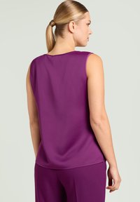 Paarse mouwloze top met een gladde textuur, ronde halslijn en lichte plooien aan de achterkant. Gecombineerd met bijpassende paarse broek.