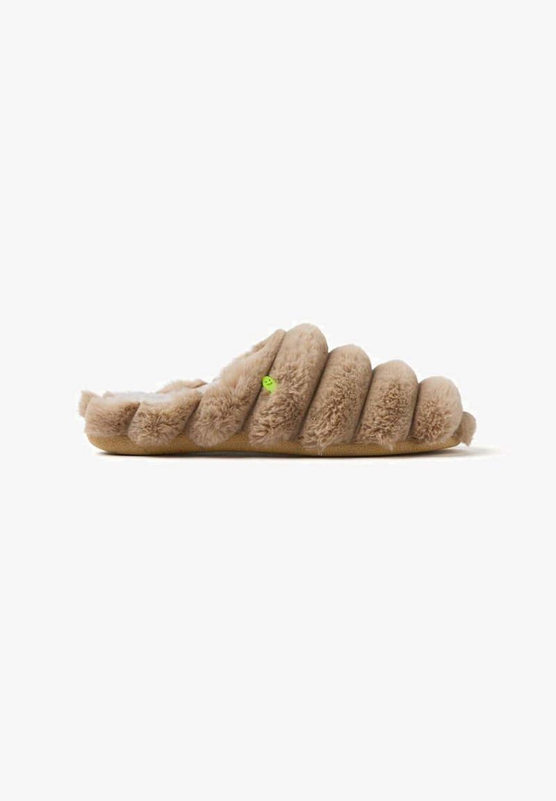 Chausson fluffy beige avec un design ondulé, un dessus textured doux et une semelle plate. Présente un petit logo vert sur le côté.