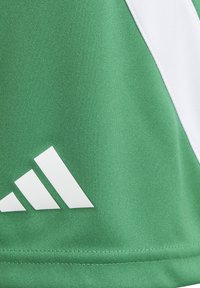 Green sports fabric with white diagonal stripe and partial white Adidas logo on textured material.