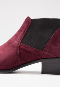 Burgundy suede ankle boot with black elastic side panels and a square block heel. Features smooth texture and contrasting material.