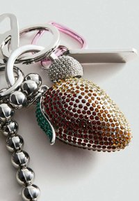 Porte-clés en forme de fraise incrusté de strass en argent, avec des accents orange, jaune et vert, attaché à des anneaux en métal argenté et rose.