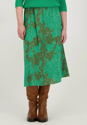 Jupe à motif floral vert avec une coupe mi-longue, associée à des bottes marron jusqu'aux genoux. Le tissu présente un mélange de teintes vertes et brunes.
