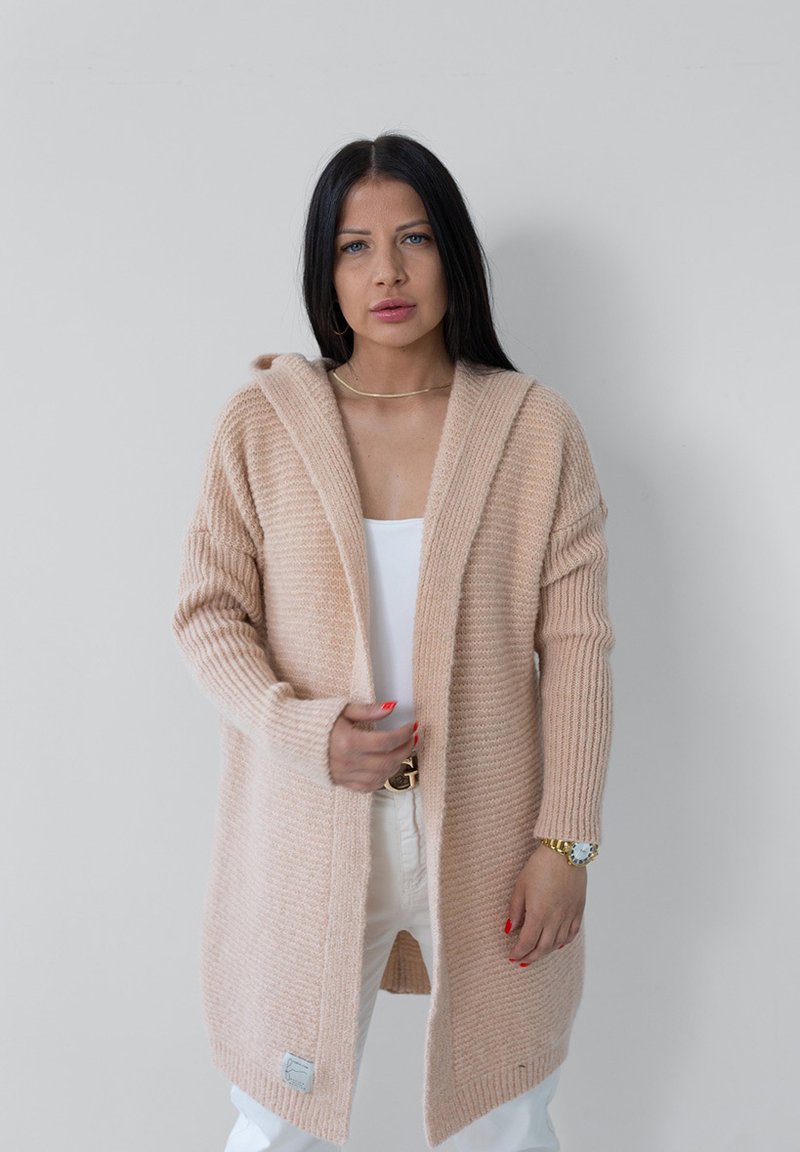 Sweter kardigan w jasnym beżu z kapturem, o prążkowanej fakturze, otwarty z przodu i z długimi rękawami. Posiada metkę z logo na hemie.
