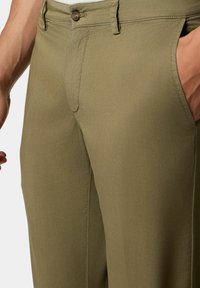 Olivově zelené kalhoty vyrobené z hladké tkaniny, s jedním knoflíkem na zapínání, bočními kapsami a slim fit střihem. Viditelná ruka u kapsy.