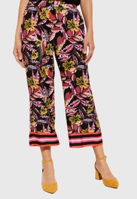 Pantalons larges à fleurs avec une base noire, ornés de feuilles et de fleurs multicolores, et d'un ourlet rayé audacieux en rouge et rose.